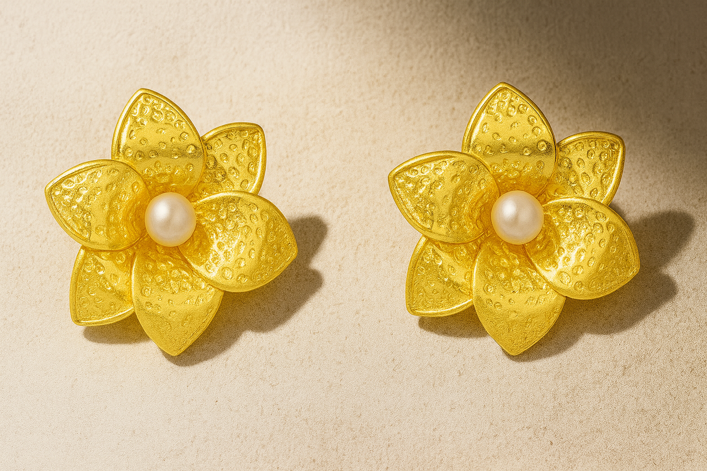Pair of gold flower-shaped earrings with pearl centers on a beige background