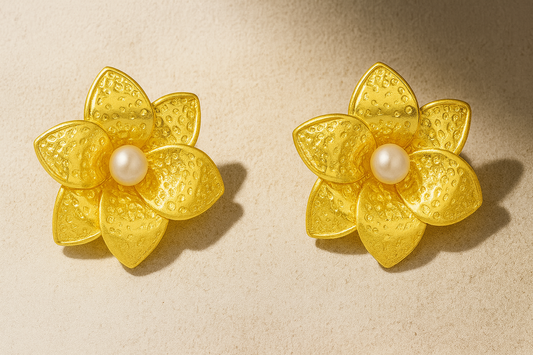 Pair of gold flower-shaped earrings with pearl centers on a beige background