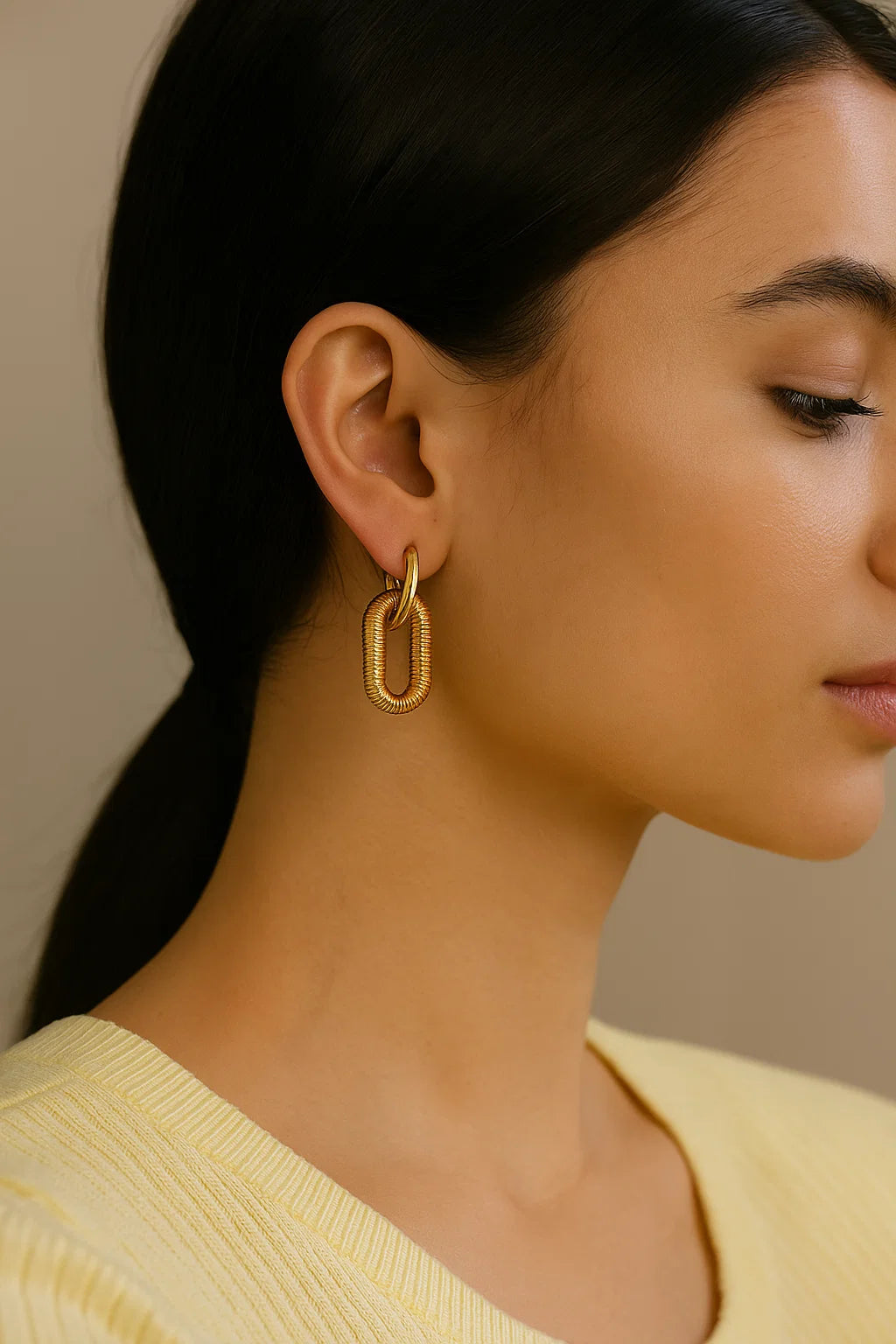 Close-up of a woman wearing gold hoop earrings with a neutral background