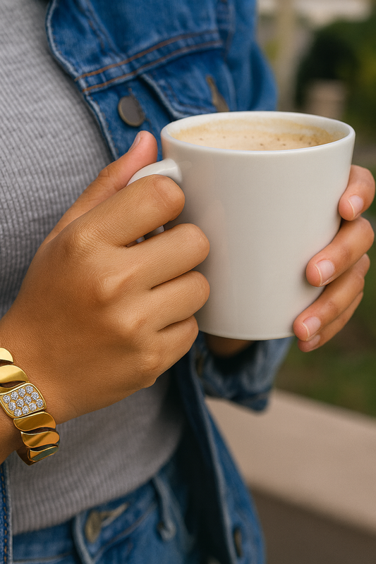 Person holding a white mug with a warm beverage, wearing a gold bracelet.
