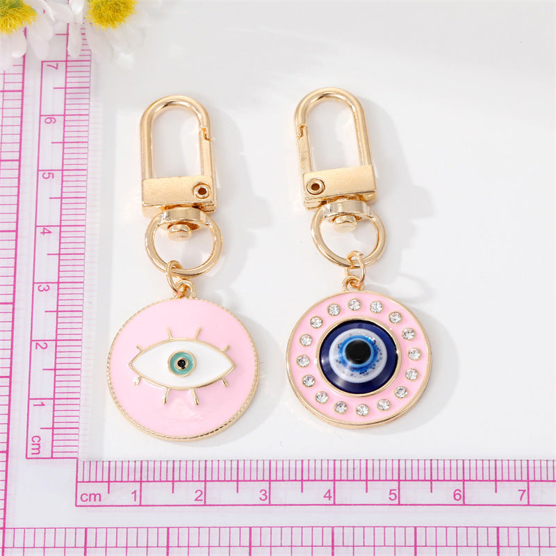 Two pink evil eye keychains with gold accents on a white background with a pink ruler.
